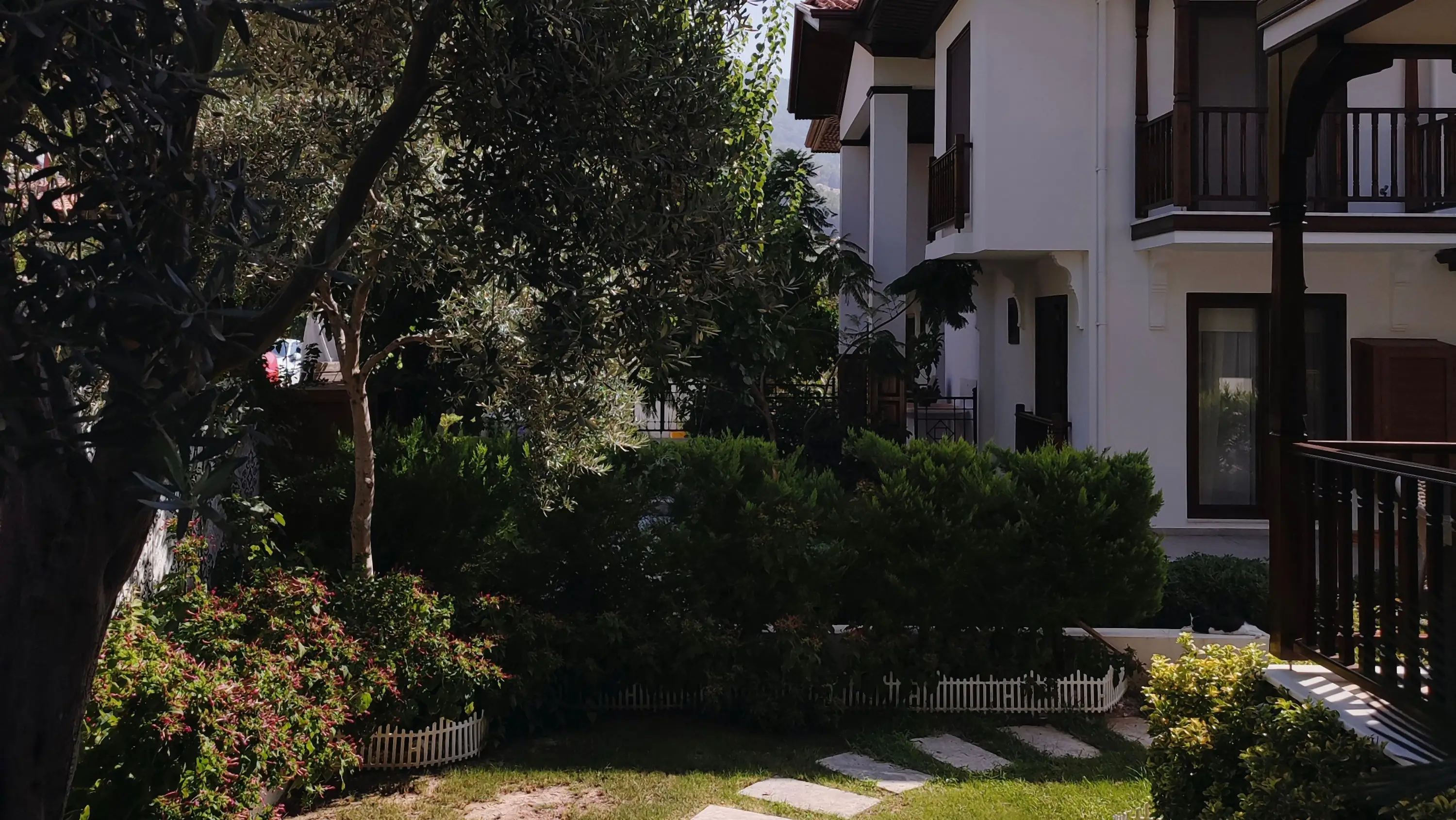 Residents crossing a shaded, landscaped path between completed low-rise buildings in the late afternoon