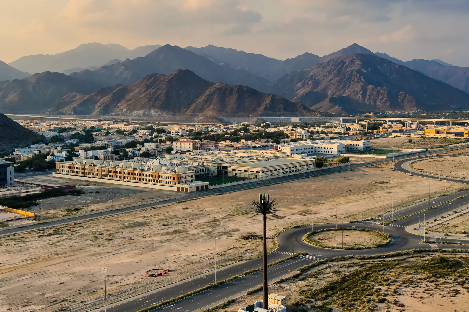 A graded but still empty tract of land, its roads already laid out, between a settlement and distant mountains