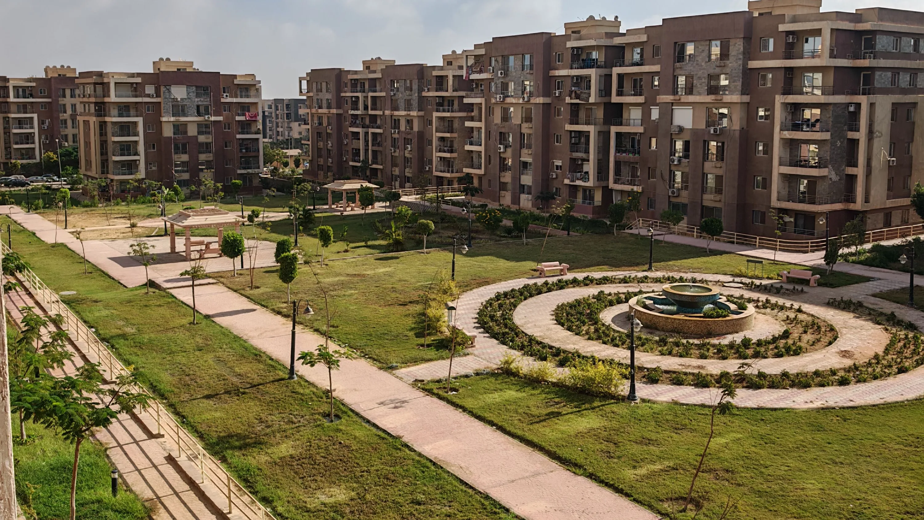 Planted lawns, footpaths and a fountain laid out between the blocks of a completed, occupied residential community